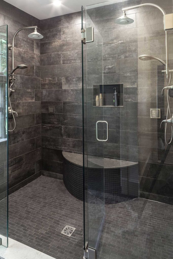 Luxurious shower in dark stone tile with multiple shower heads and a bench seat