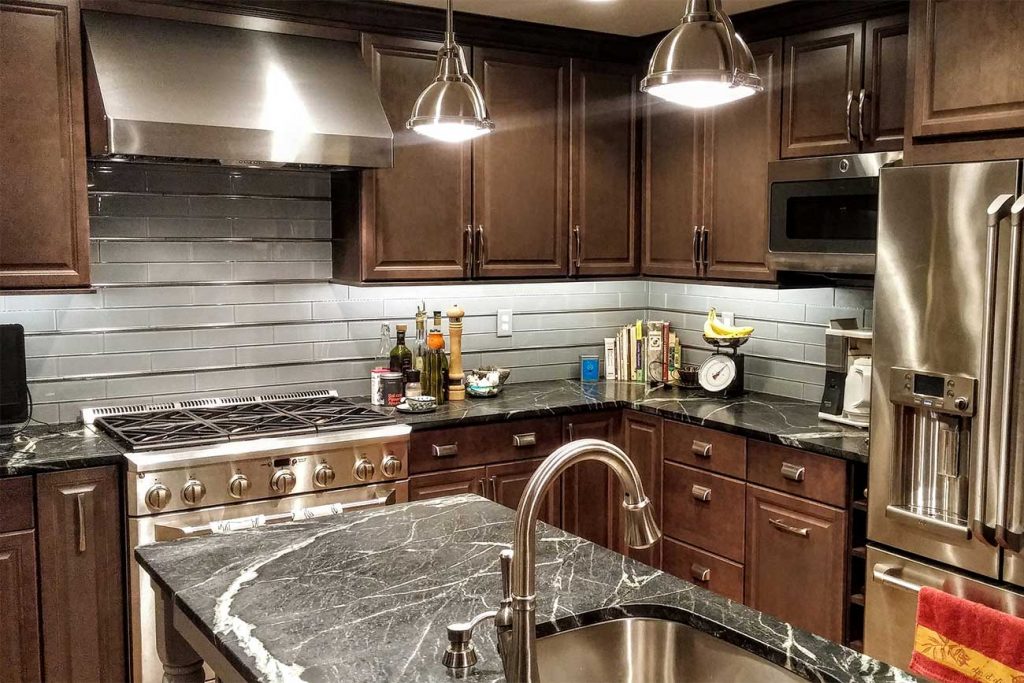 Kitchen with rich wood cabinets, grey glass backsplash tile, and soapstone countertop material.
