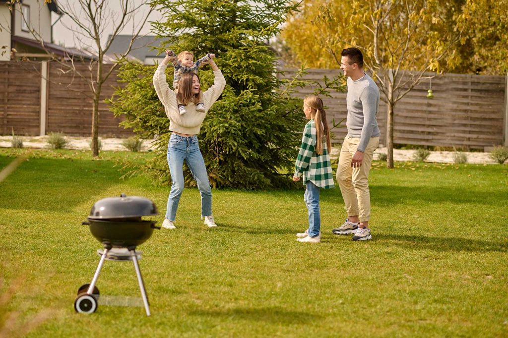 family playing in yard with small charcoal grill in grass
