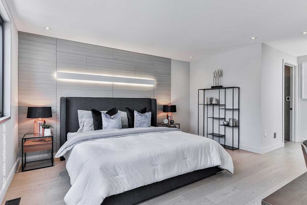 Minimalist design in bedroom, painted white with a light gray accent wall and simple furnishings.