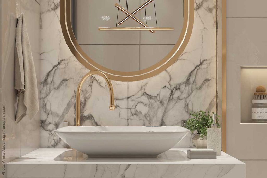 Glamorous powder room design with unique gold bar chandelier, gold framed mirror, and marble backsplash