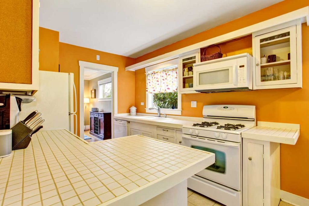 Time to remodel - outdated kitchen with white tile countertops, orange walls, and very old appliances