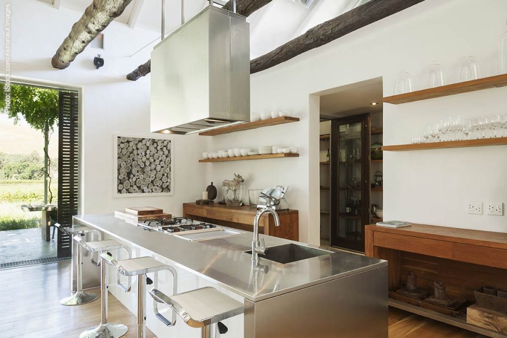 Industrial-style kitchen with metal countertop on island and vent hood, wooden cabinets and open shelves