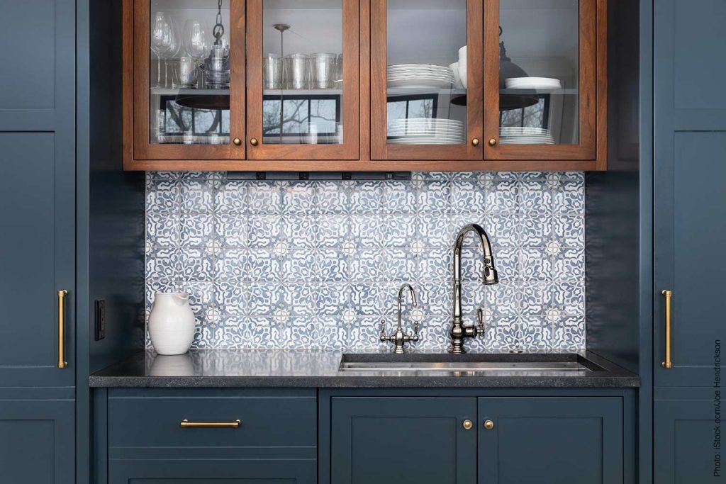 Add color to your home like this kitchen with a beautiful pattern tiled backsplash, black granite countertops, and surrounded by blue and wood cabinets.
