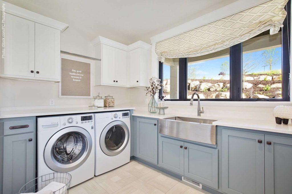 Laundry room with light blue and gray cabinets with beautiful view out oversized windows