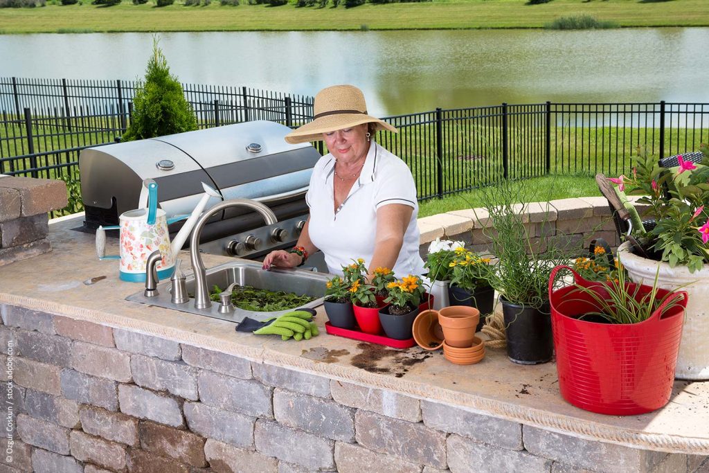 Woman standing in her outdoor kitchen backyard space cleaning fresh vegetables